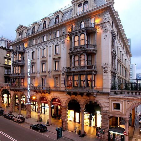 Hotel Bristol Palace Genoa Exterior photo The photo shows a grand hotel building, likely the Hotel Bristol. It features an elegant architectural design with ornate details, including balconies and decorative moldings. The façade is illuminated, giving it a warm glow in the evening light. The