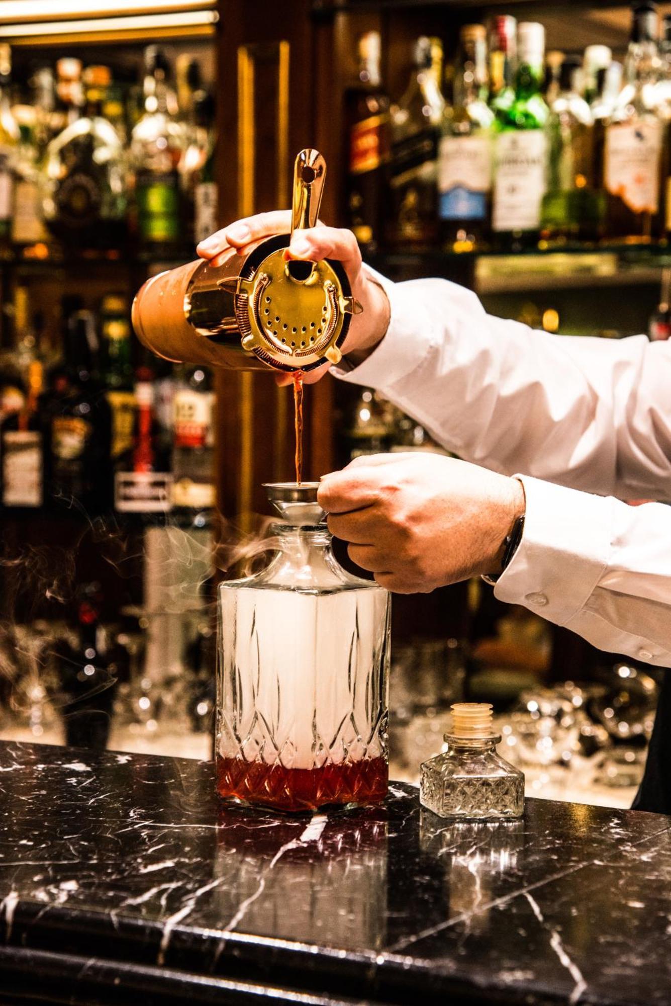 Hotel Bristol Palace Genoa Exterior photo The photo shows a bartender pouring a liquid from a cocktail shaker into a glass bottle or decanter. The bartender is holding a strainer over the bottle to catch any solid particles, ensuring a smooth pour. The background displays various bottles of 