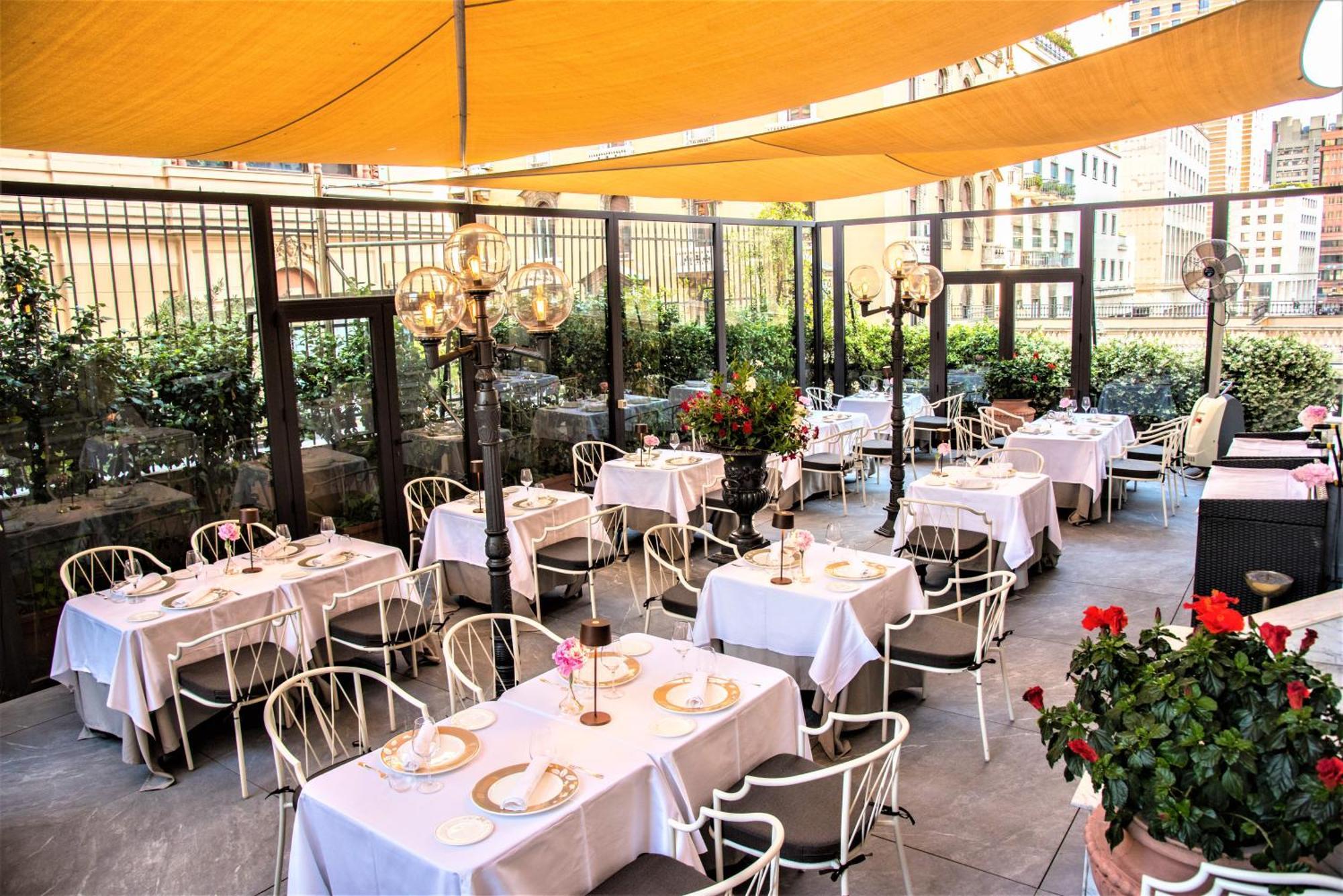 Hotel Bristol Palace Genoa Exterior photo The photo shows a stylish outdoor dining area of a restaurant, featuring several tables covered with white tablecloths. Each table is elegantly set, with plates and centerpieces, enhancing the atmosphere. The space is shaded by a large yellow canopy,