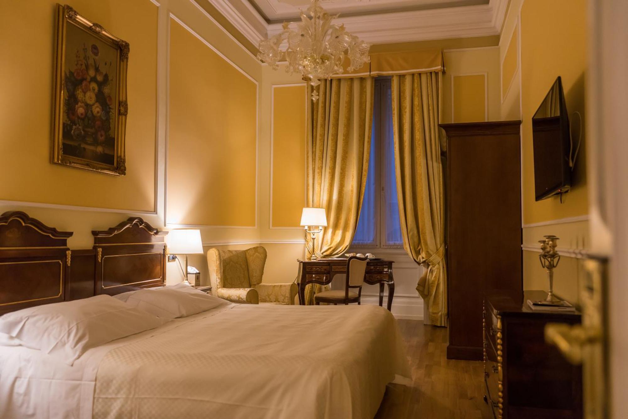 Hotel Bristol Palace Genoa Room photo The photo shows a beautifully designed bedroom with warm yellow walls. There is a large bed with a white bedspread positioned against one wall. Next to the bed, there are two table lamps providing soft lighting. A cozy seating area is visible, featur