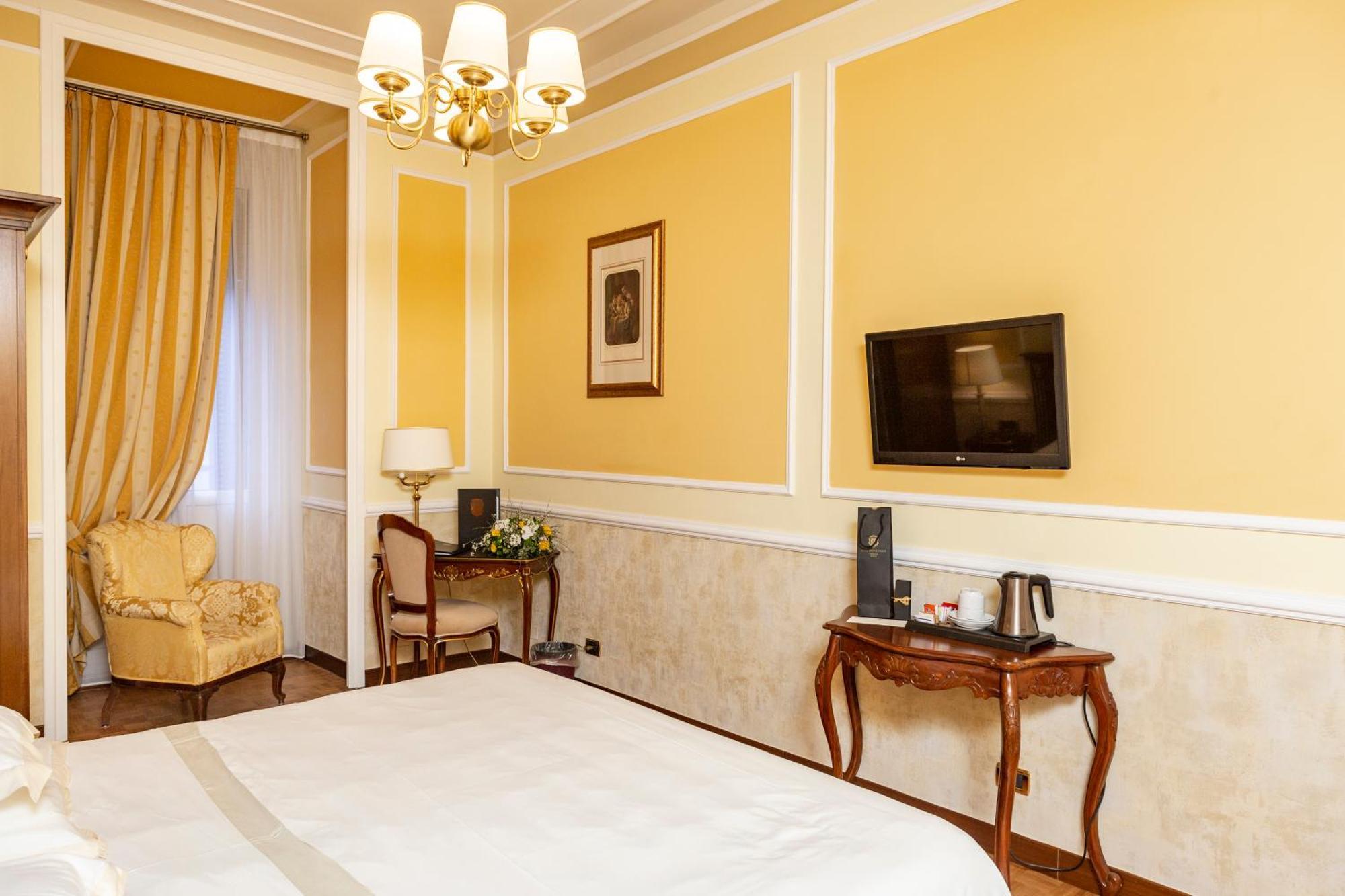 Hotel Bristol Palace Genoa Room photo The photo shows an interior of a hotel room. The walls are painted a warm yellow color, and there's a chandelier hanging from the ceiling. On one side, there's a large window draped with elegant curtains. A comfortable armchair is situated in the cor