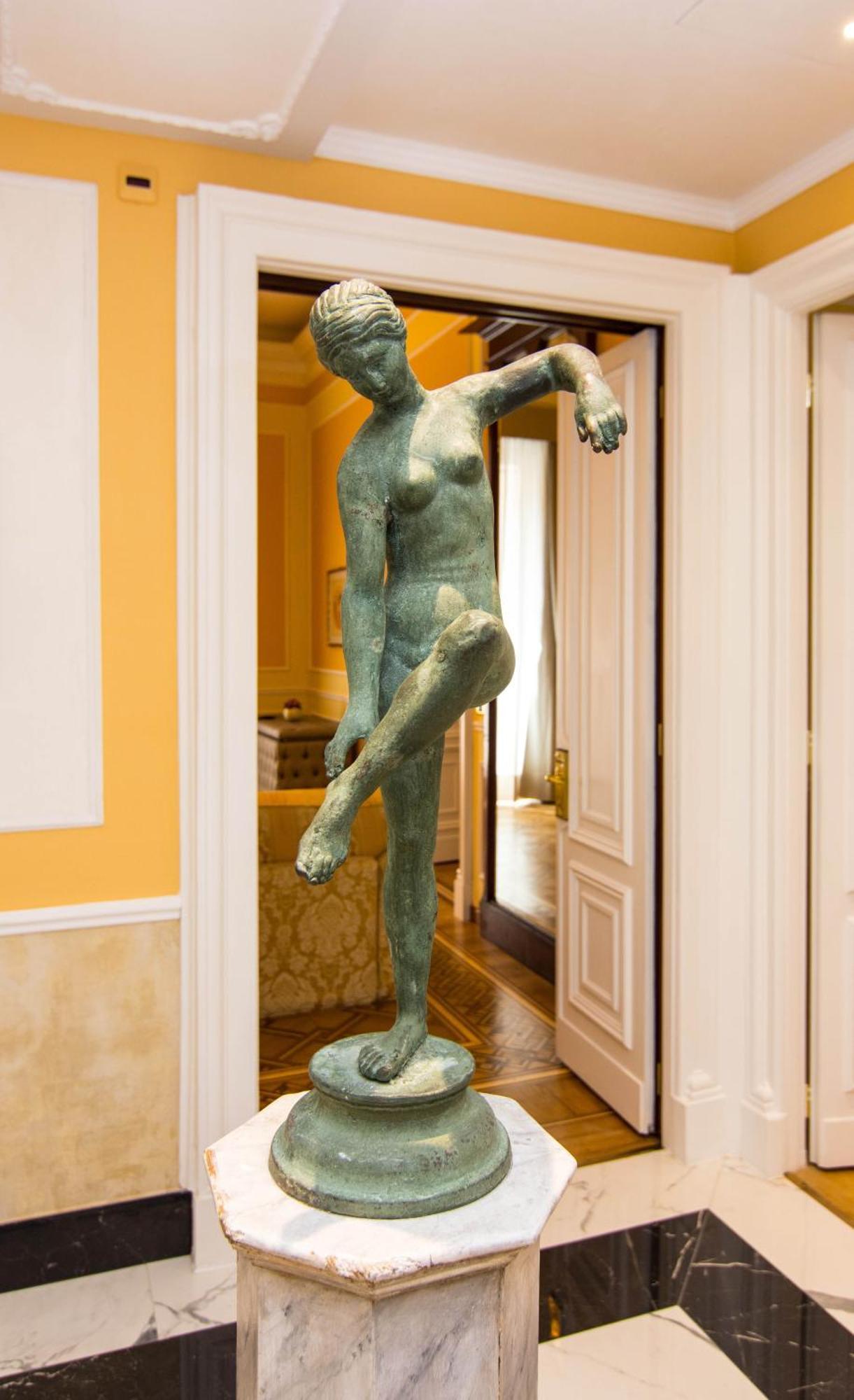 Hotel Bristol Palace Genoa Exterior photo The photo shows a sculpture of a female figure displayed in an interior space. The sculpture is made of a greenish material, likely bronze, and depicts the figure in a pose with one arm raised and one leg lifted. The surroundings include light-colore