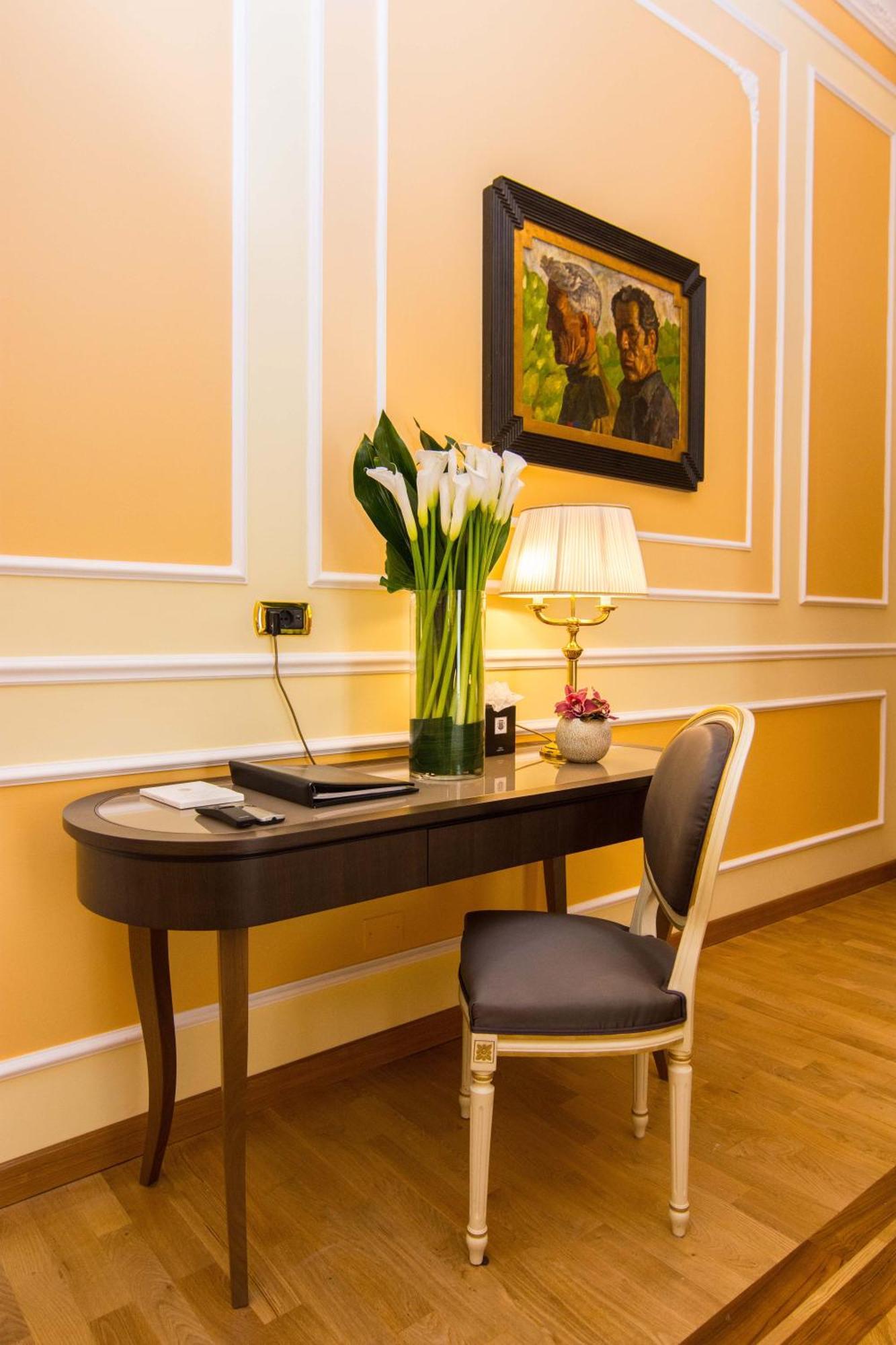 Hotel Bristol Palace Genoa Exterior photo The photo shows a stylishly arranged corner of a room. There is a sleek, curved desk made of dark wood positioned against a softly colored wall. On the desk, there is a black folder and a small decorative item, possibly a flower pot. A tall, elegant 