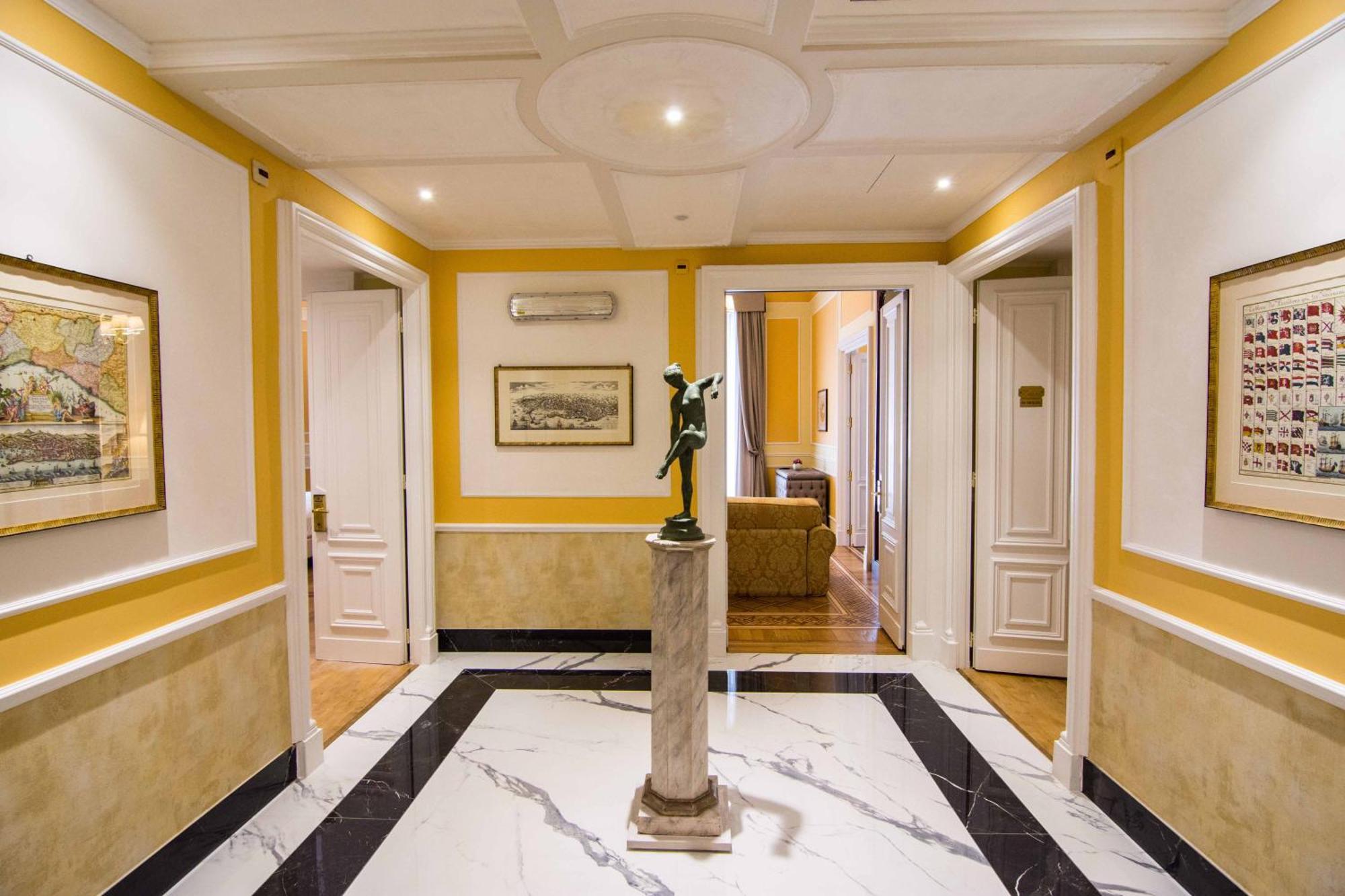 Hotel Bristol Palace Genoa Exterior photo The photo shows an elegant hallway with a bright yellow wall and marble flooring. The ceiling is detailed, featuring a circular design. In the center, there is a statue on a small pedestal, adding a decorative touch to the space. The walls are adorne