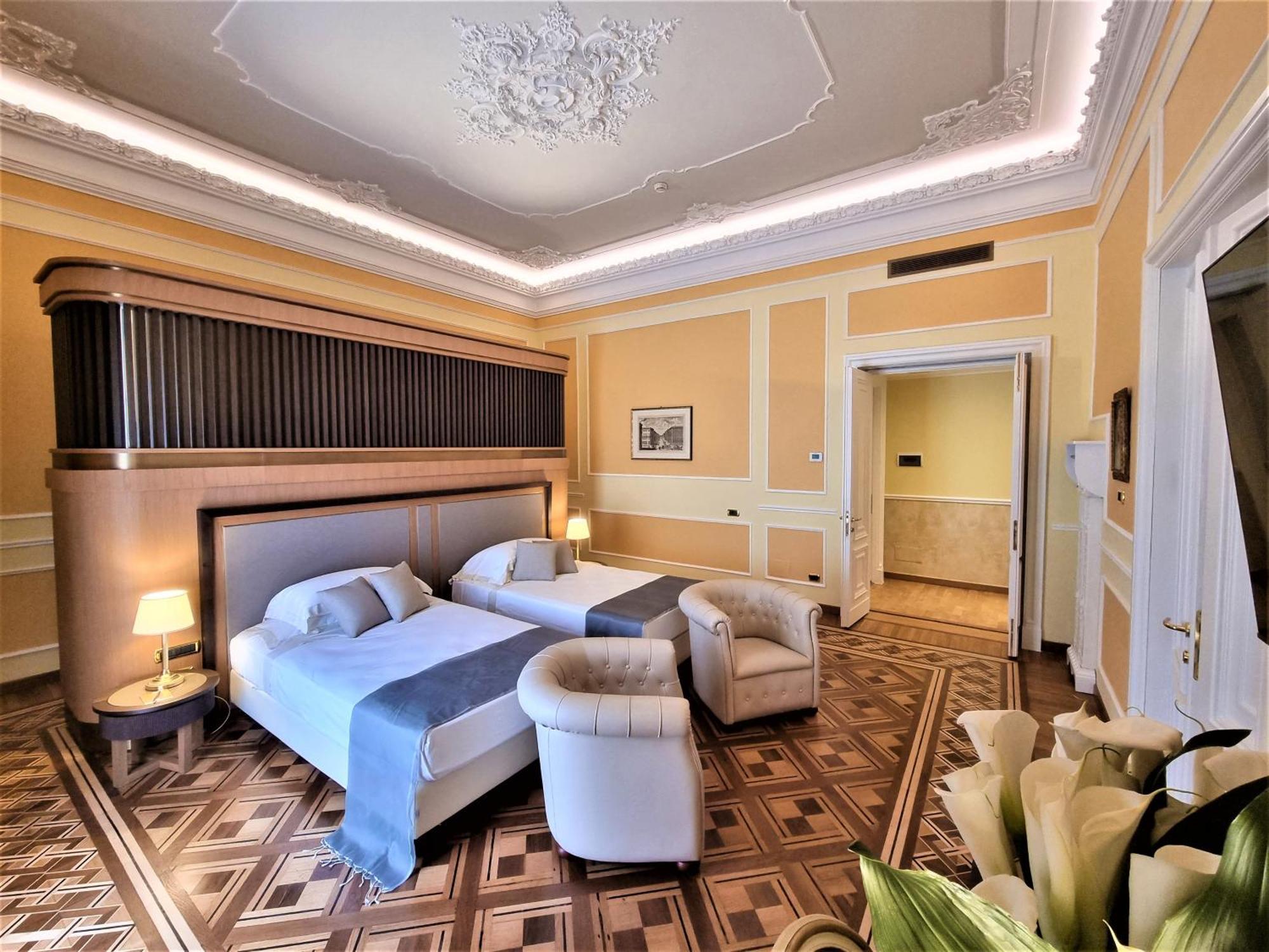 Hotel Bristol Palace Genoa Exterior photo The photo shows a well-appointed hotel room featuring two beds, a comfortable armchair, and elegant decor. The walls are painted a soft yellow, and the ceiling boasts ornamental detailing. There are lamps by the beds providing warm lighting, and the 