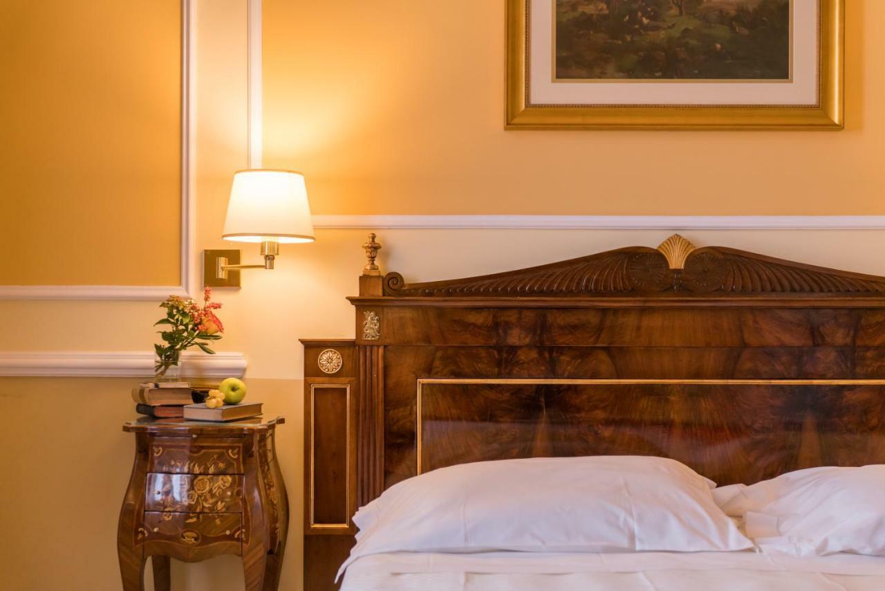 Hotel Bristol Palace Genoa Exterior photo The photo shows a cozy and elegant bedroom. The walls are painted a warm yellow, enhancing the inviting atmosphere. There is a large wooden bed with a decorative headboard in the foreground, made up with white bedding. Next to the bed is a small side